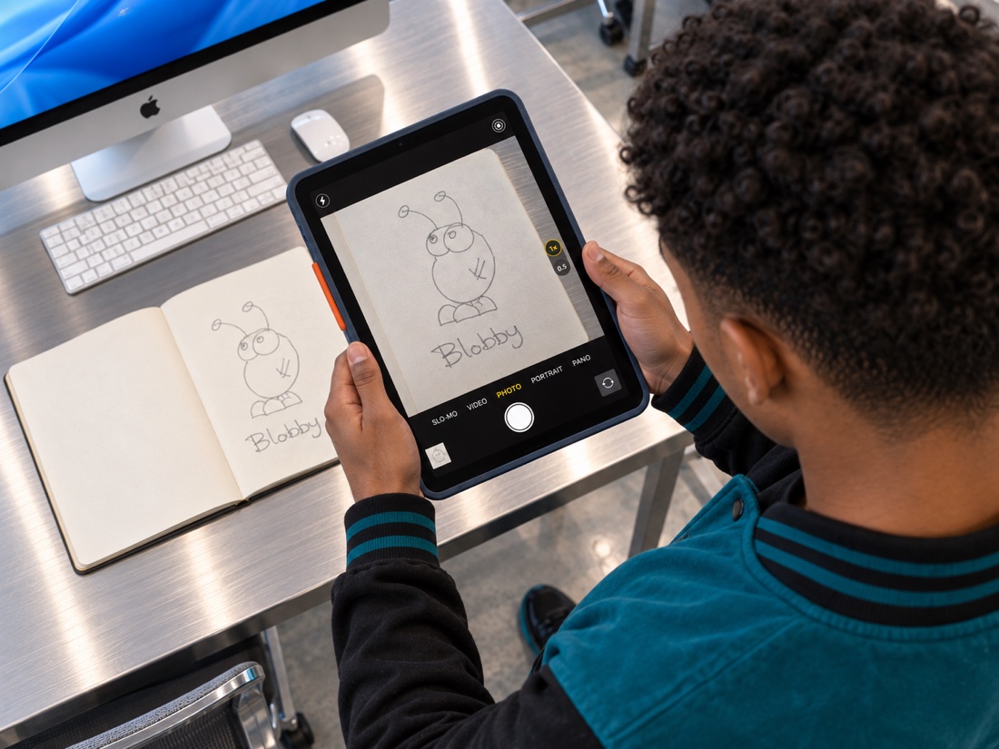 A student photographing a finished sketchbook character named Blobby with an iPad