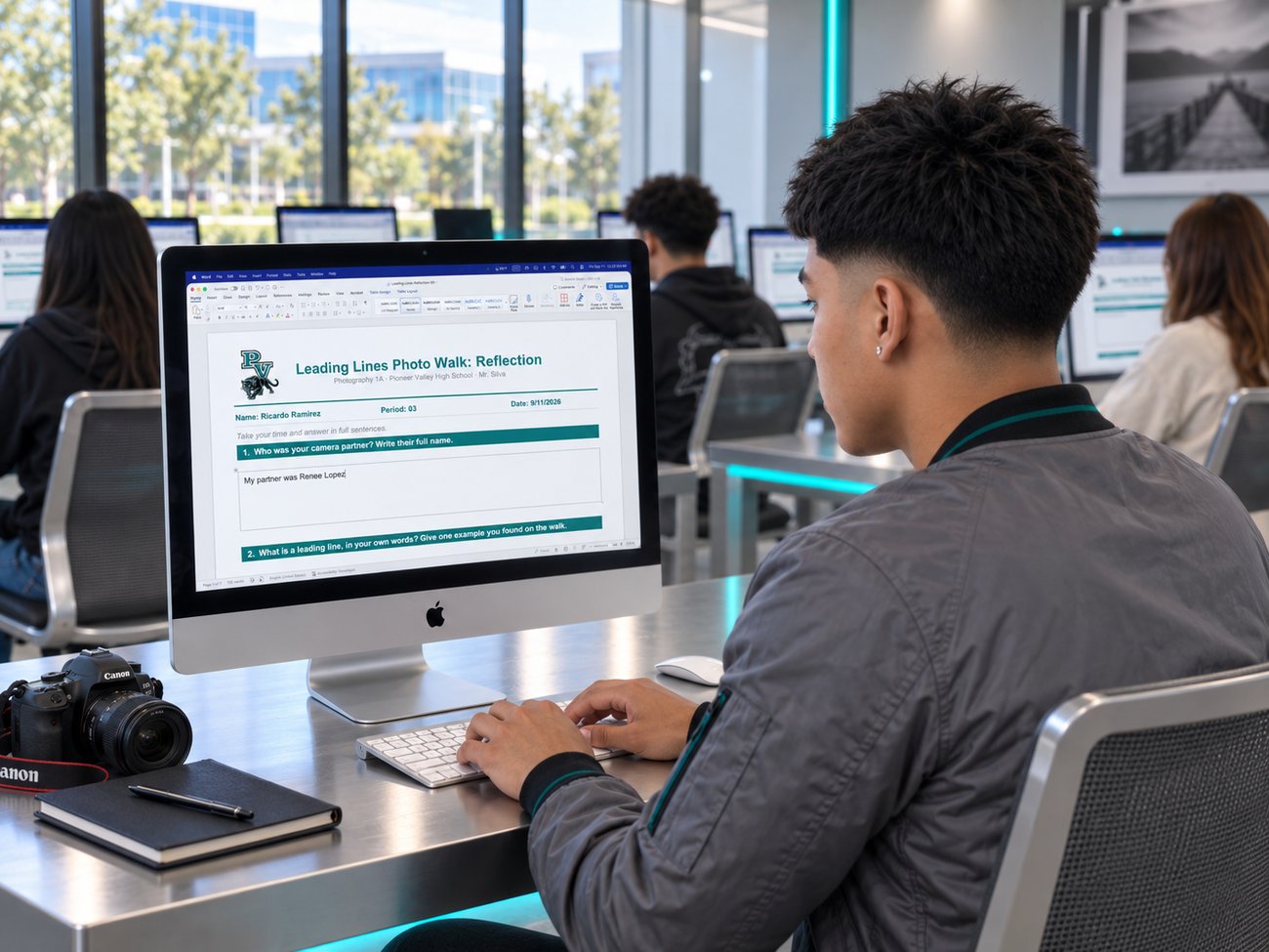 A Pioneer Valley student typing his Leading Lines reflection in the Word document on an iMac in the lab, a Canon camera on the desk
